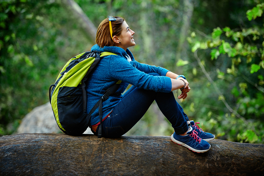 Woman hiker smiling standing outside in forest with backpack
